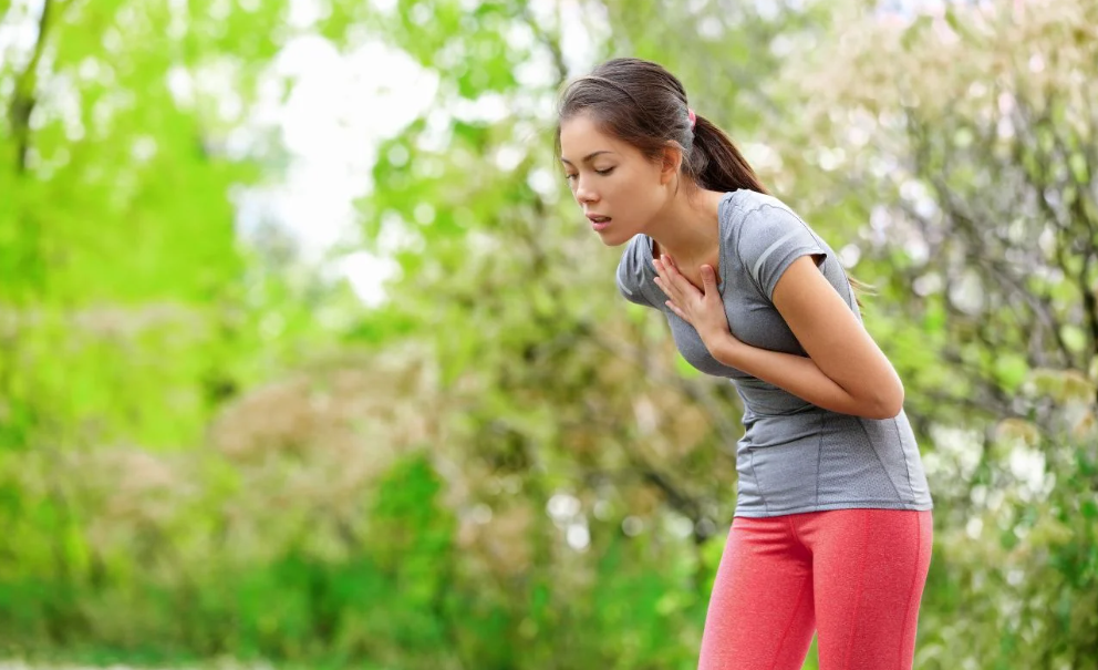 A woman experiences acid reflux while running in a park.